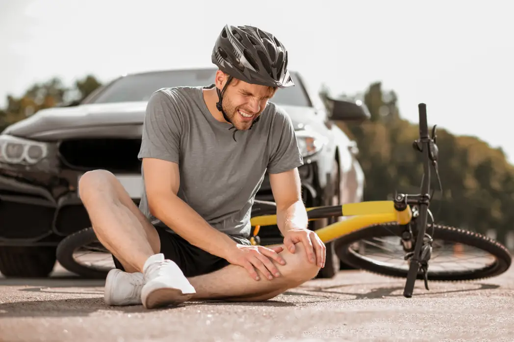 kneeinjuryyoungadultinjuredcyclisthelmetsittingholdingkneeroadnearfallenbikefrontcar Bridgewater Law Group