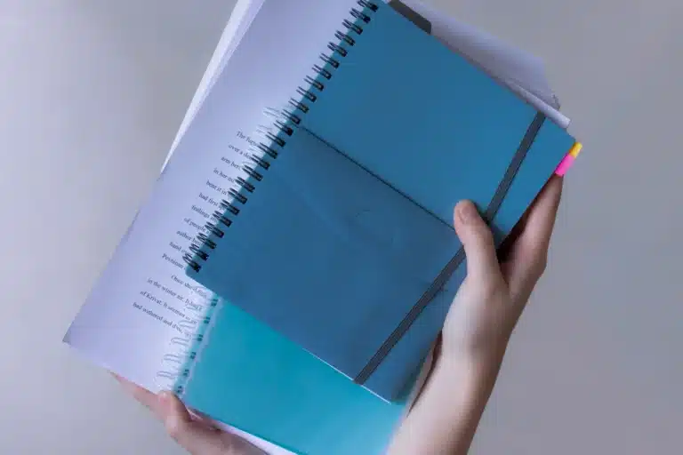 Hands holding blue notebooks and a stack of papers.