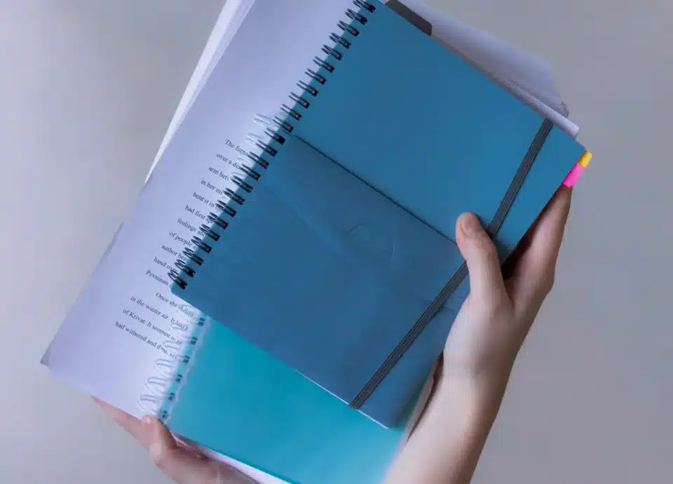 Hands holding blue notebooks and a stack of papers.